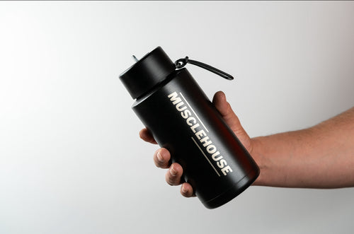Hand holding a black Muscle House Australia water bottle, perfect for staying hydrated during workouts and fitness activities.